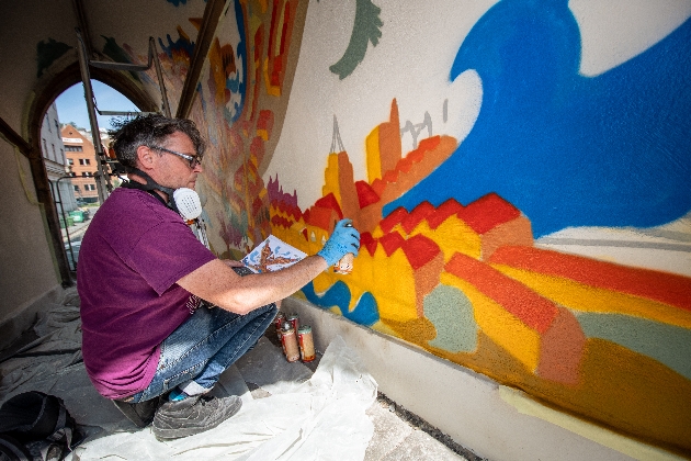 Artist Andy Council painting in red roofs on the mural in Broad Street