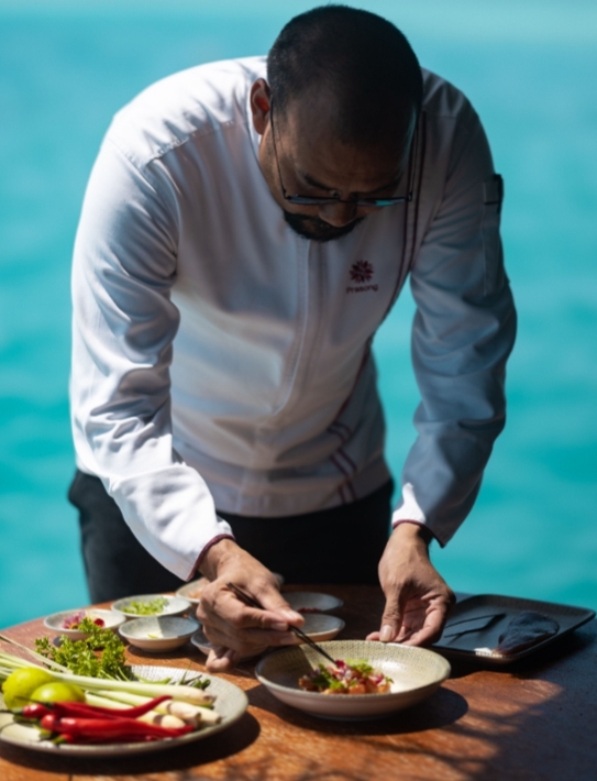 Man in chefs jacket serving food by the water 