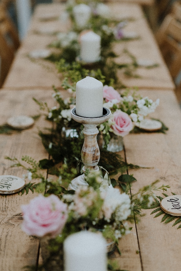 rustic wedding tablescape with white candles, pink flowers and log slice place names. Banquet style layout