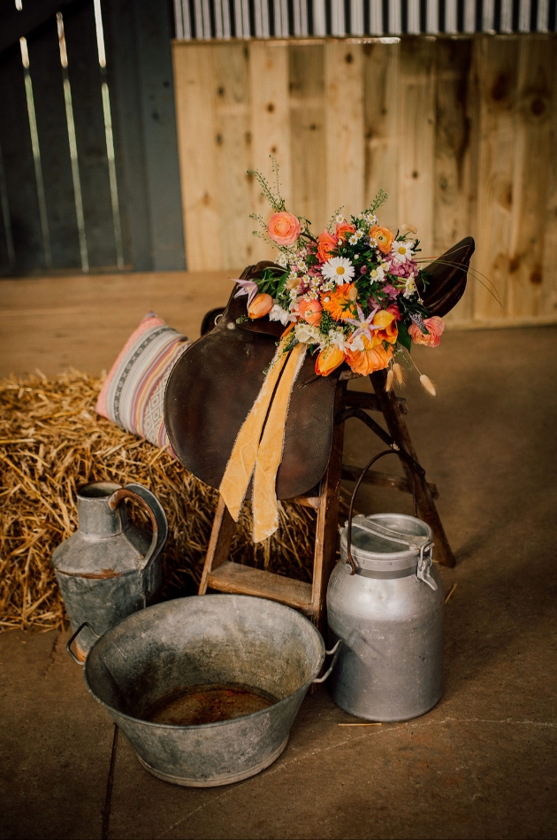 saddle decorated with orange flowers and surrounded by milk churns. Western Luxe wedding look.