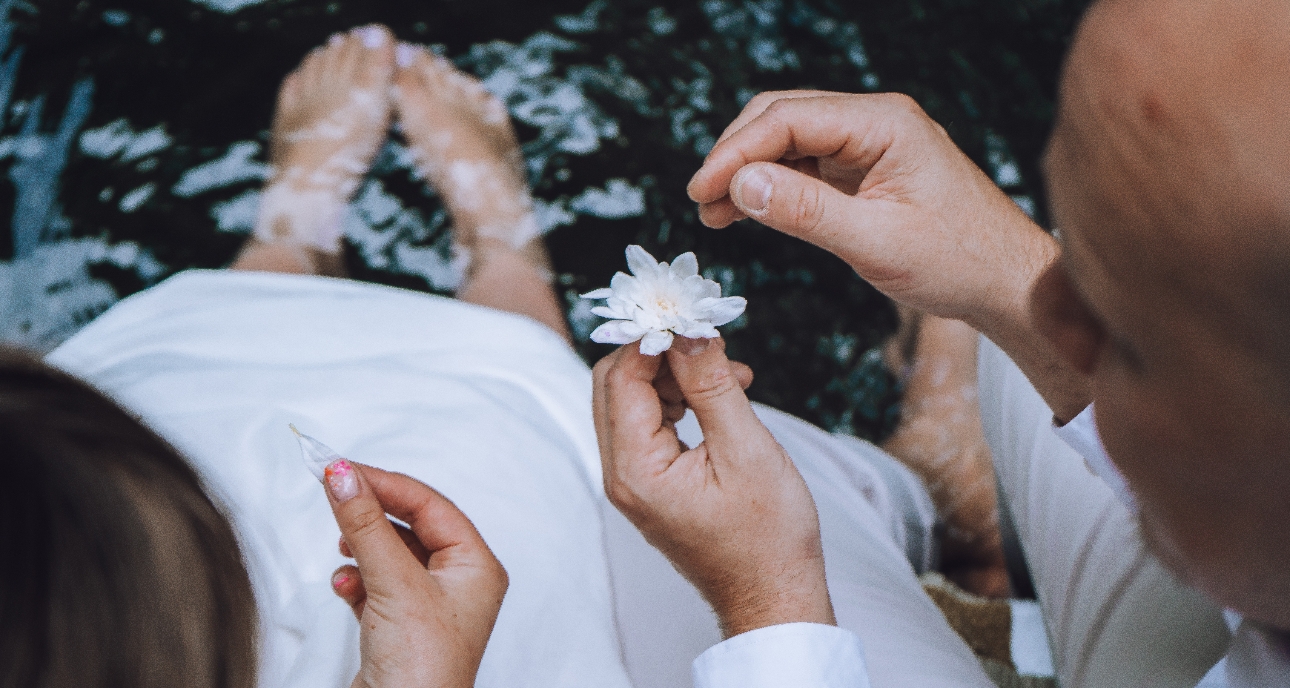 Shot from behind couple with the feet in a stream looking at a white flower