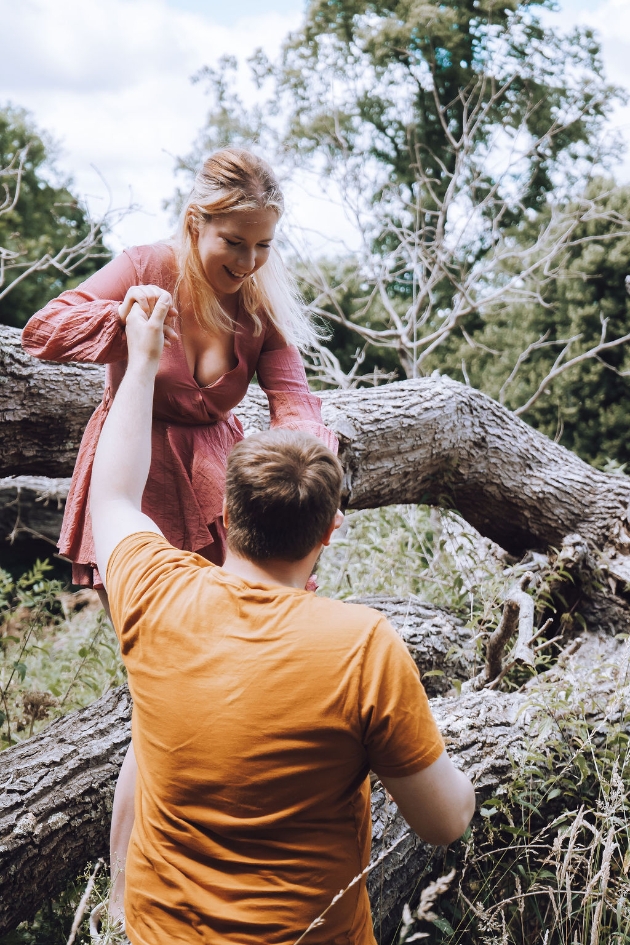 couple in the woods, man is helping woman down from a log