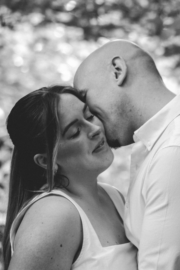 Engaged couple in the woods - he kisses her on the cheek - black and white image