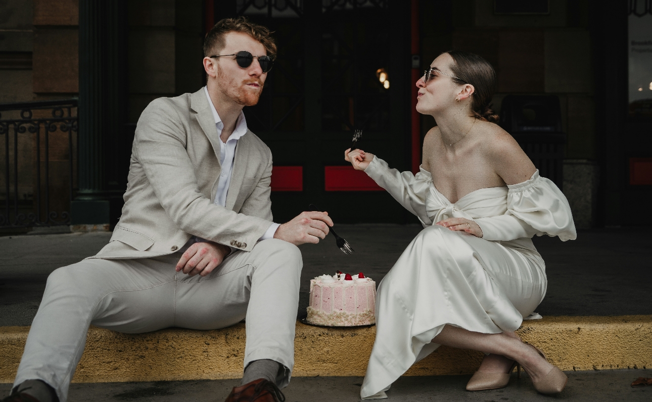 bride and groom sitting on the curb eating wedding cake