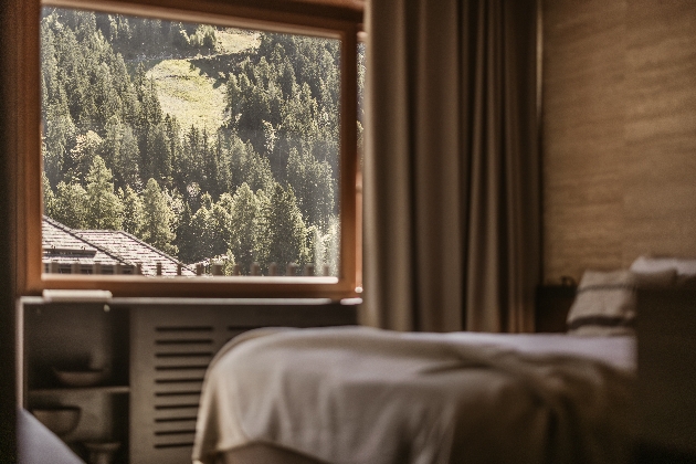 A bed with a window nearby that shows beautiful views of a forest